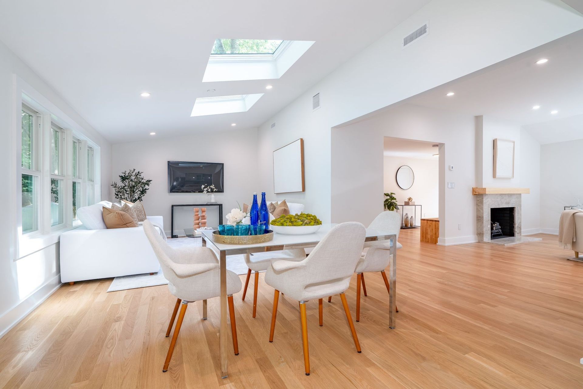 Modern living and dining area with skylights, wooden floors, and a cozy fireplace.