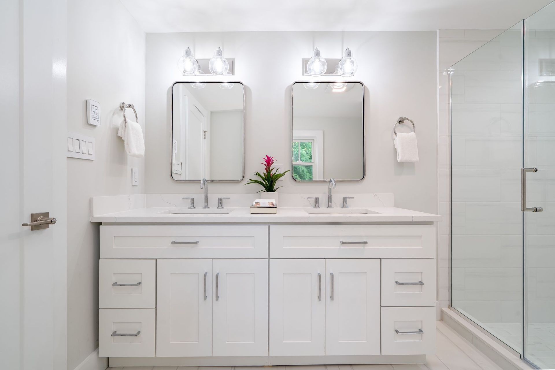 Modern bathroom with double sinks, mirrors, and a glass-enclosed shower.