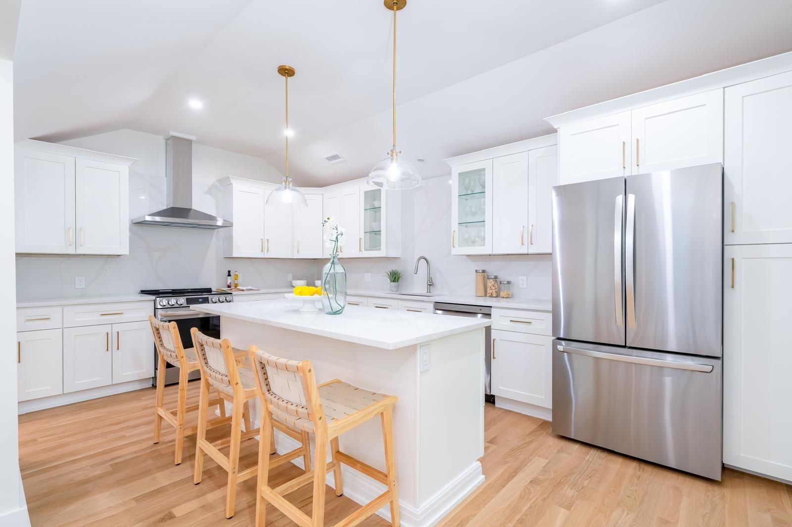 Modern kitchen with white cabinets, stainless steel appliances, and a central island with wooden chairs.